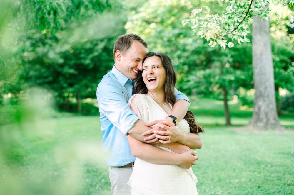 A joyful couple embracing in a sunlit garden with lush green trees in the background.
