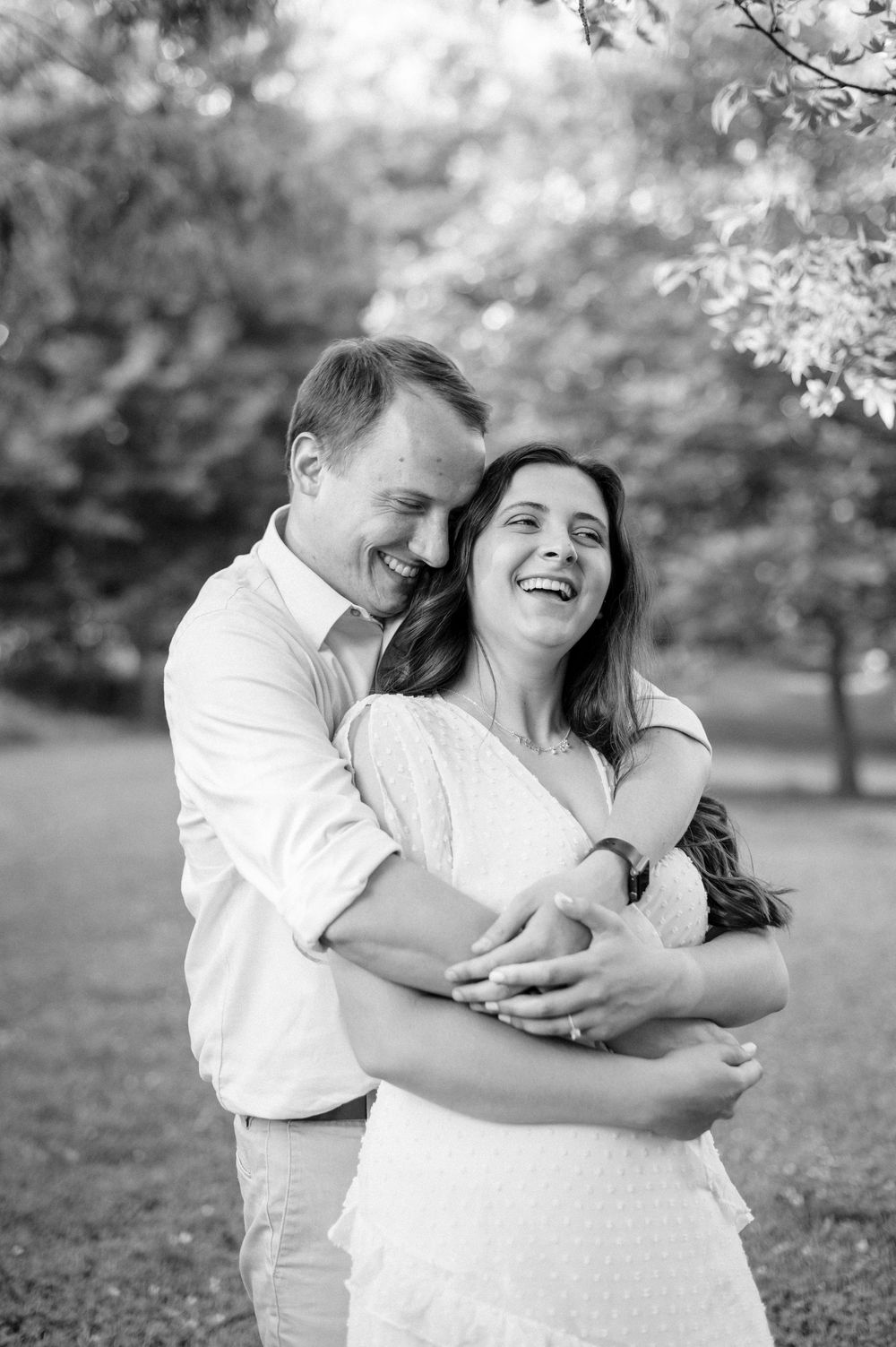 A black and white photo of a couple laughing together in a park setting.