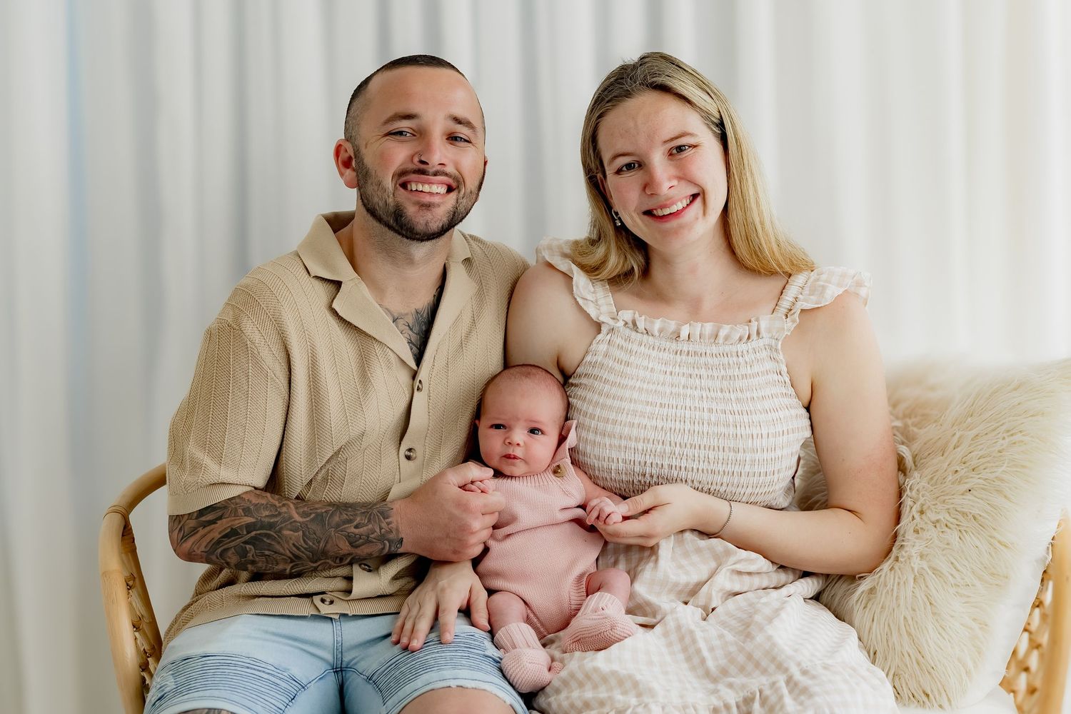 A smiling family of three sits together against a white backdrop during an indoor portrait photography session.