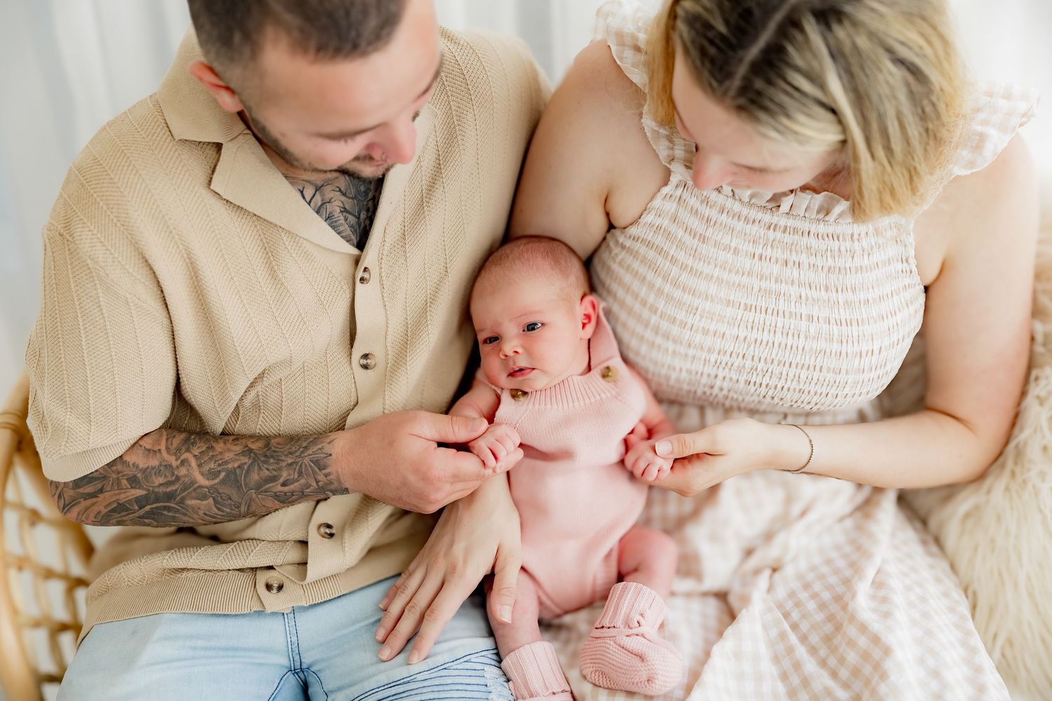 Parents in casual attire hold and gaze lovingly at their newborn baby during an intimate indoor photo session.