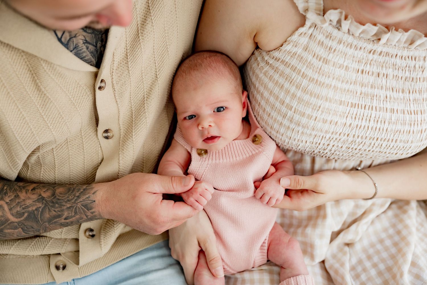 A tender moment as parents share a close embrace with their newborn baby on a soft bed.