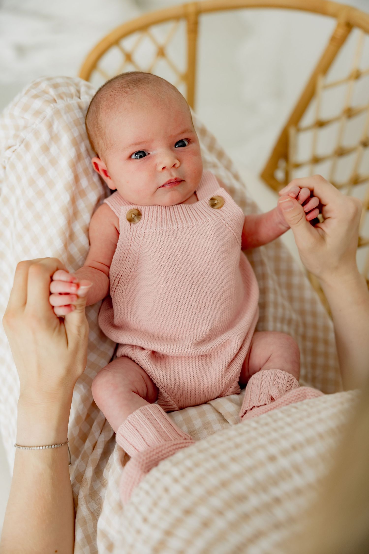 Baby wearing soft pink knit romper sits on checkered fabric while being held by adult hands.