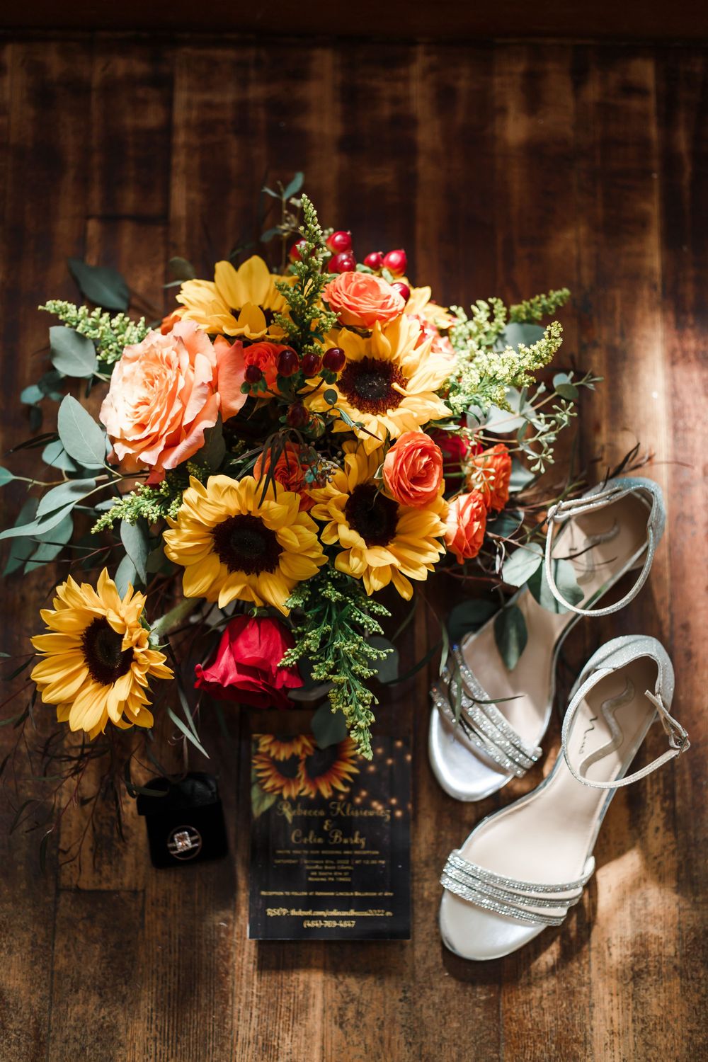 Wedding details with sunflowers and roses arranged with white bridal shoes on wooden surface.