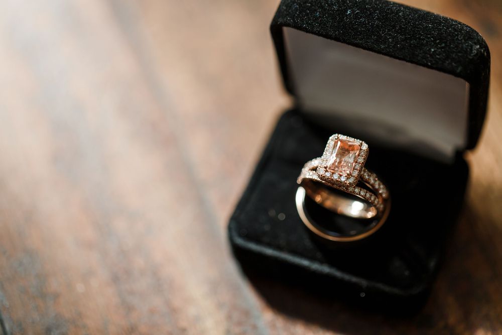 A sparkling diamond engagement ring sits elegantly in a black velvet jewelry box on a wooden surface.