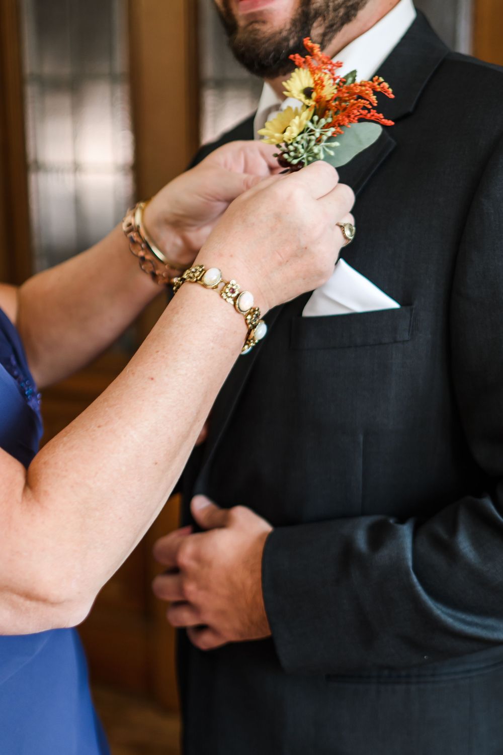 Hands pinning a fall-colored boutonniere onto a black suit jacket.