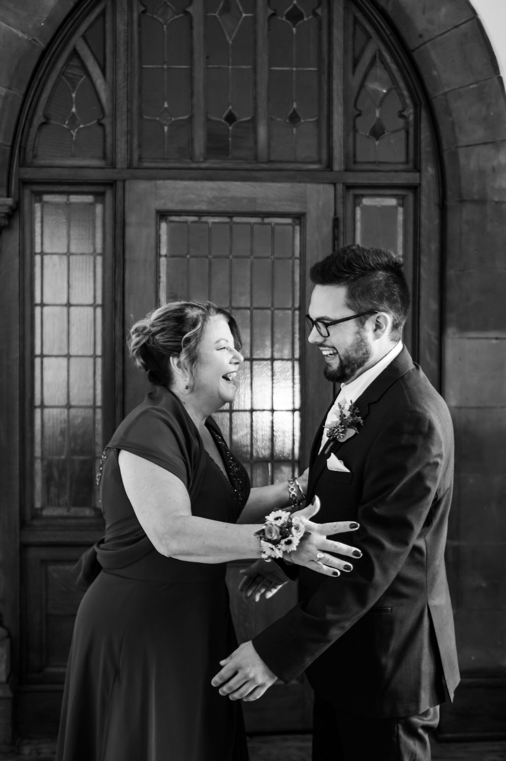 Emotional black and white wedding moment captured in front of gothic windows.