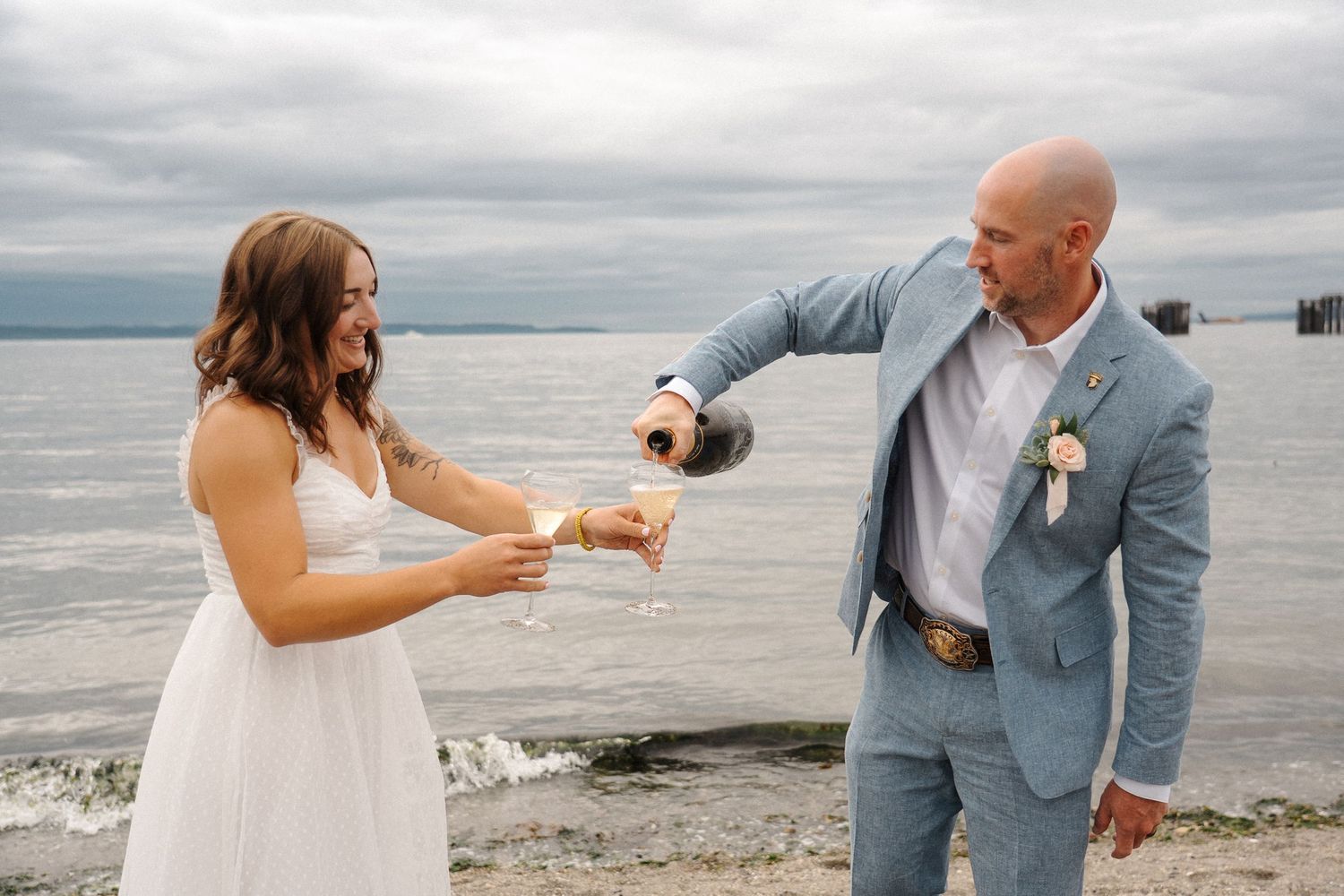 A romantic series of beach engagement photos showing a couple sharing pizza and champagne by the ocean at sunset.