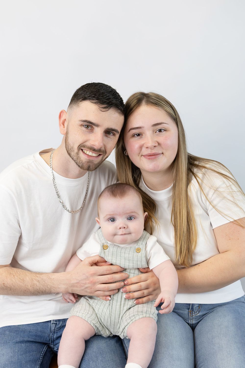 A family wearing white tops and jeans poses together in a series of casual studio portraits.
