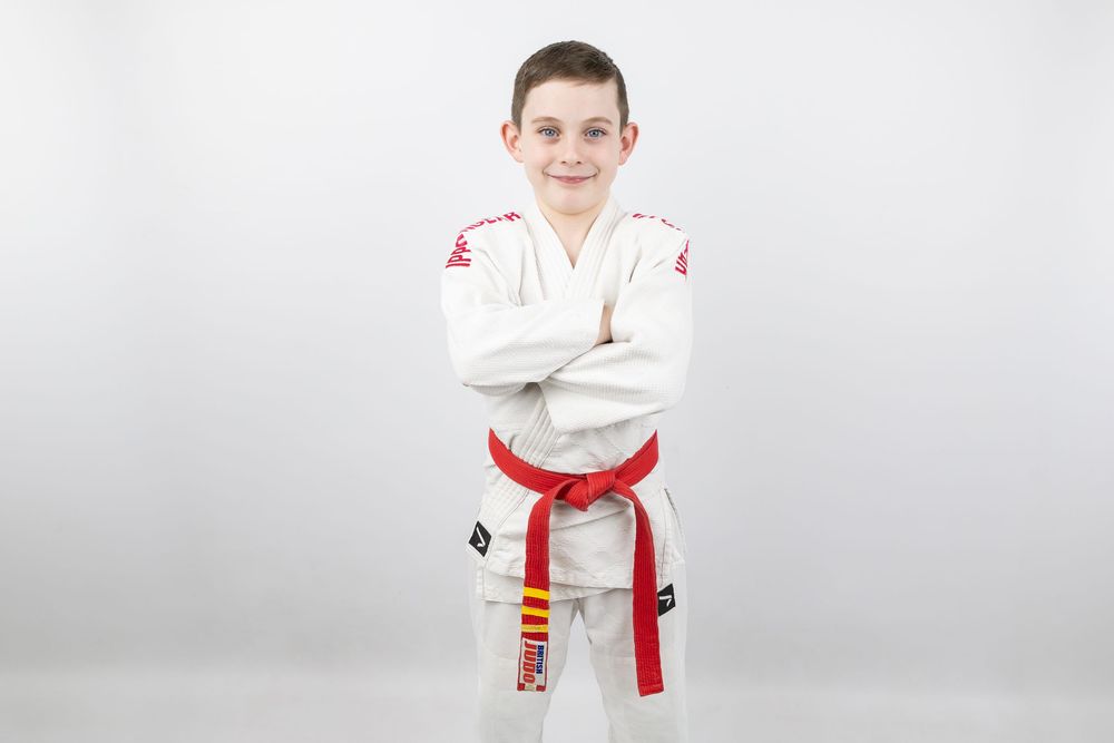Young martial artist in white karate uniform with red belt standing confidently.