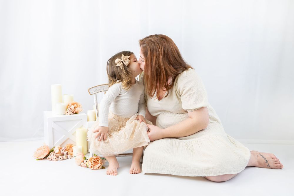 Mother and child in white dresses lying together on light background with soft decor.