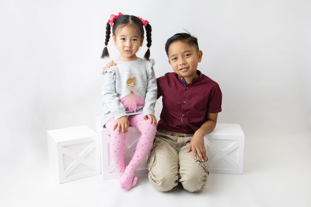 Two children sitting together on white background in casual attire.