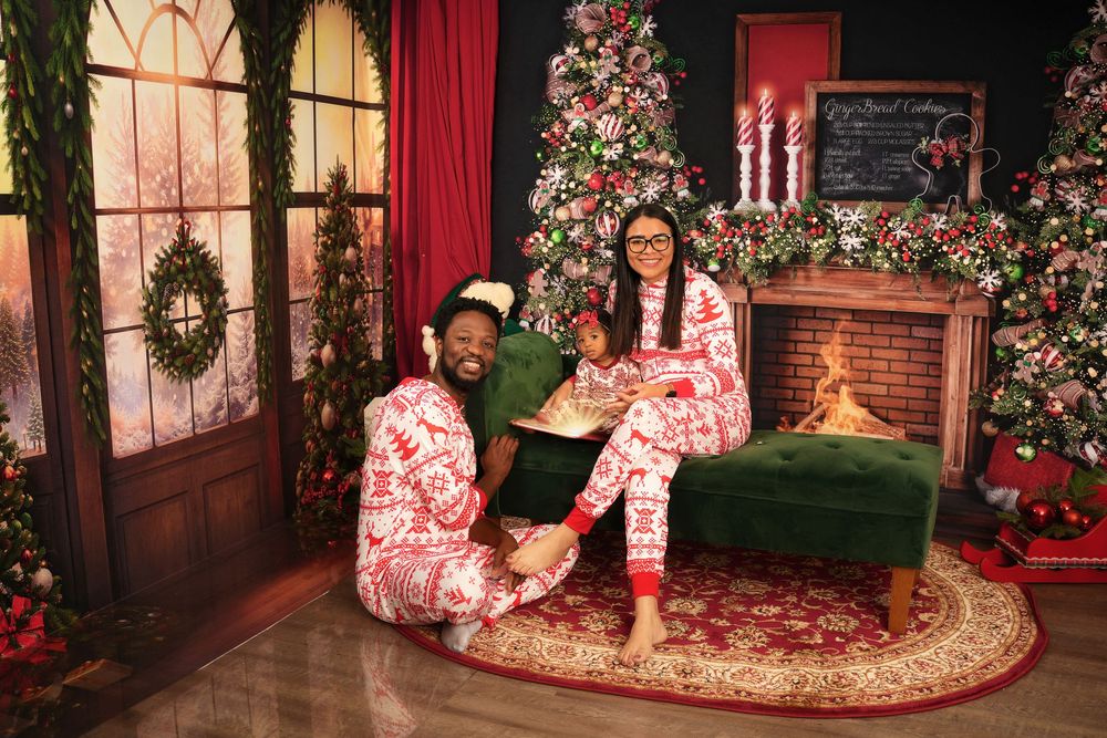 A festive Christmas photo session setup with decorated tree, red curtains, and brick wall backdrop in a studio.