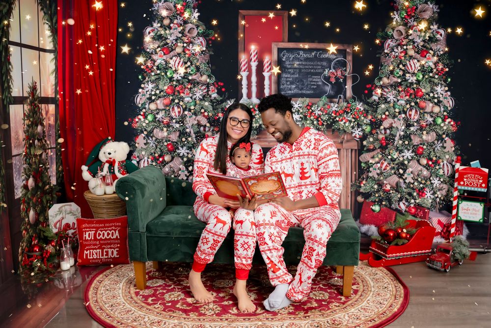 A festive holiday scene with two people in matching pajamas sitting by decorated Christmas trees surrounded by presents and lights.