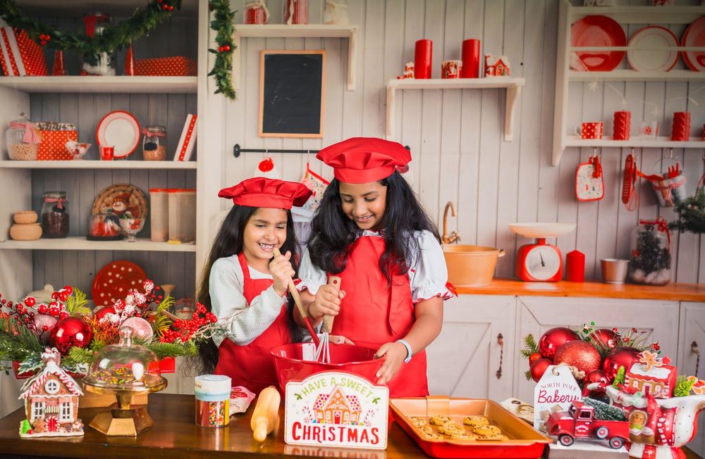 Two people in matching red outfits bake cookies together in a festively decorated kitchen with holiday accents.