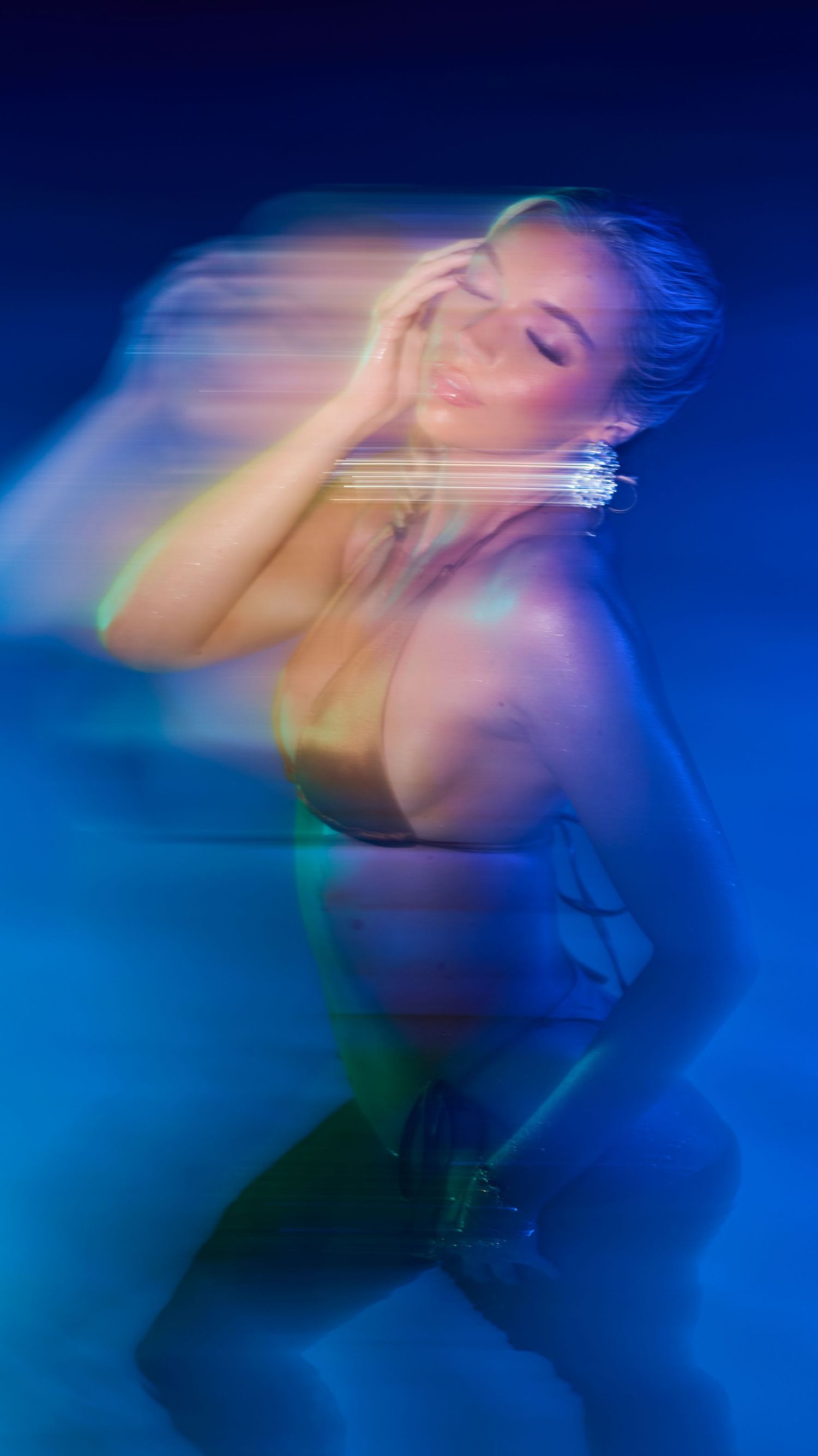 Artistic motion blur portrait in blue tones shows figure with closed eyes in a dreamy ethereal pose with holographic effects.