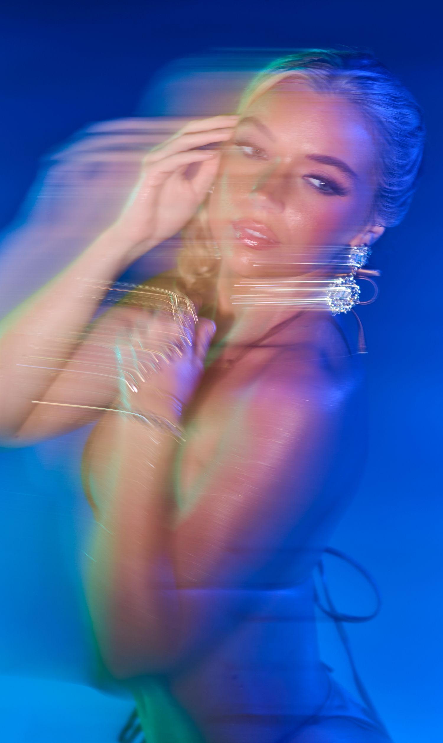 Dreamy artistic portrait with motion blur effect in blue lighting showing sparkly earrings and bracelet jewelry accessories.