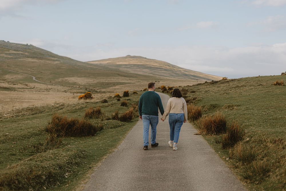 Couple walking hand in hand on a winding path through rolling hills.
