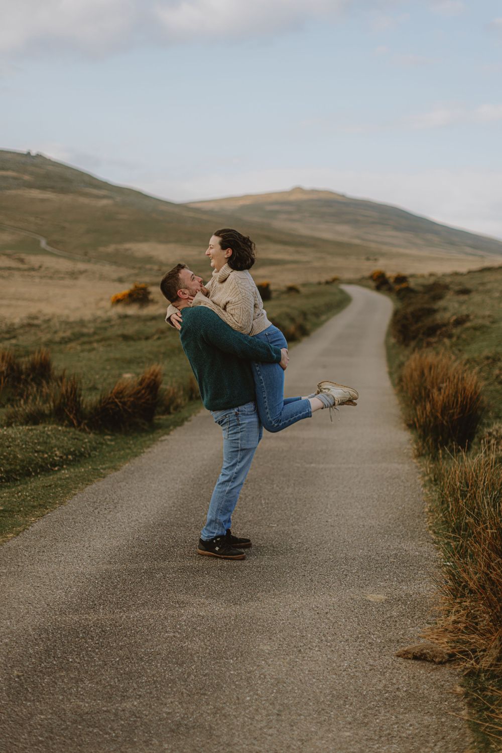 Joyful couple sharing a playful lift moment on a countryside path.