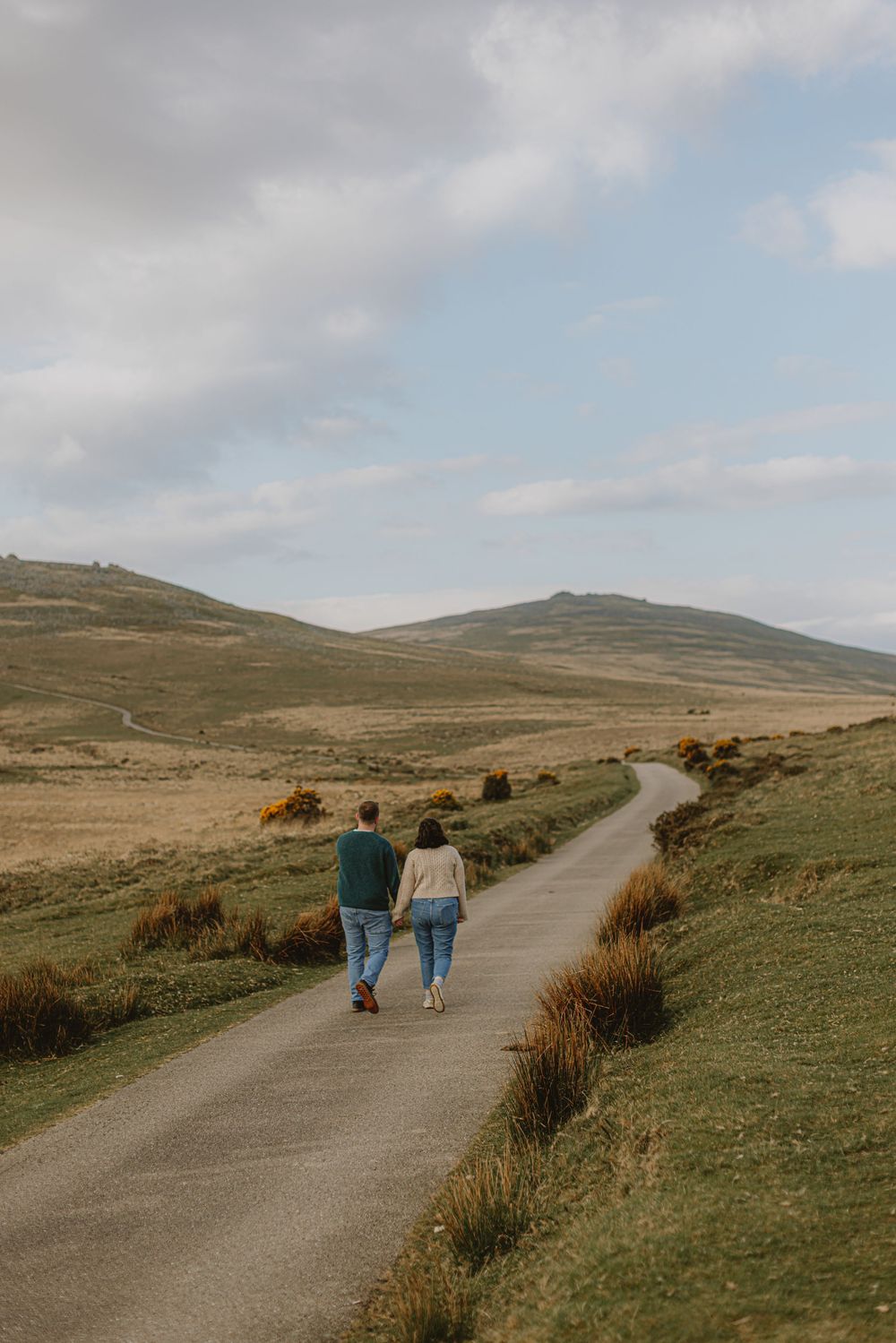 Couple walking along a winding path through scenic moorland landscape.