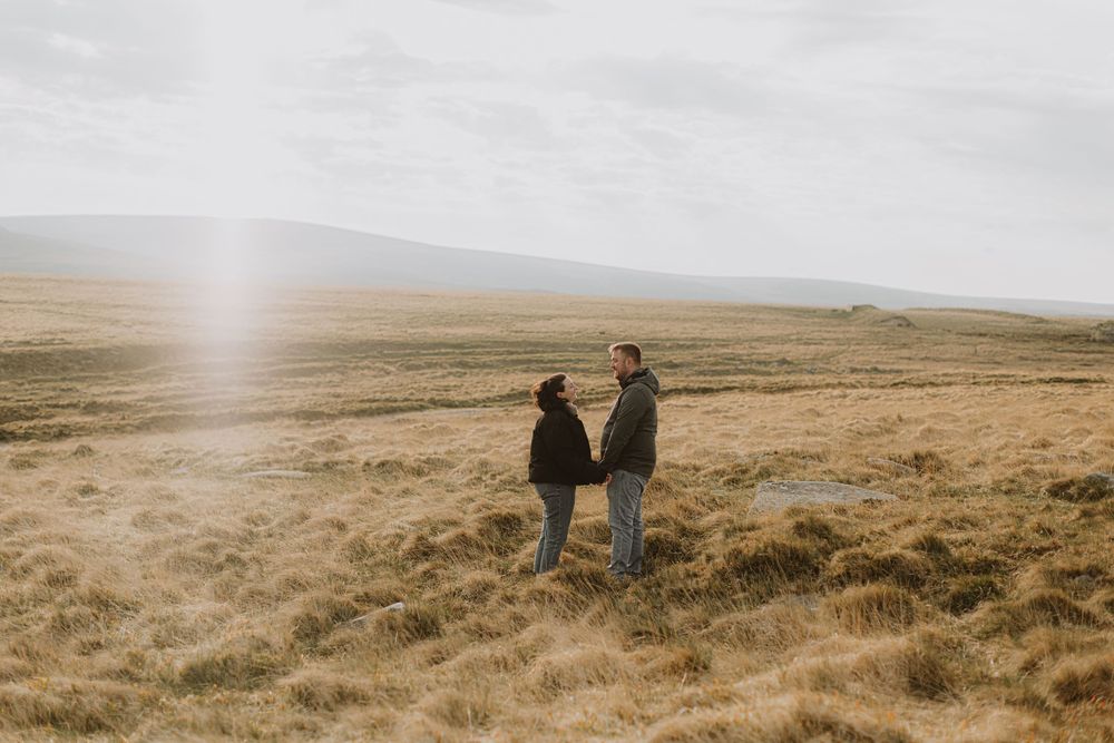 Two people standing together on misty moorland during golden hour.