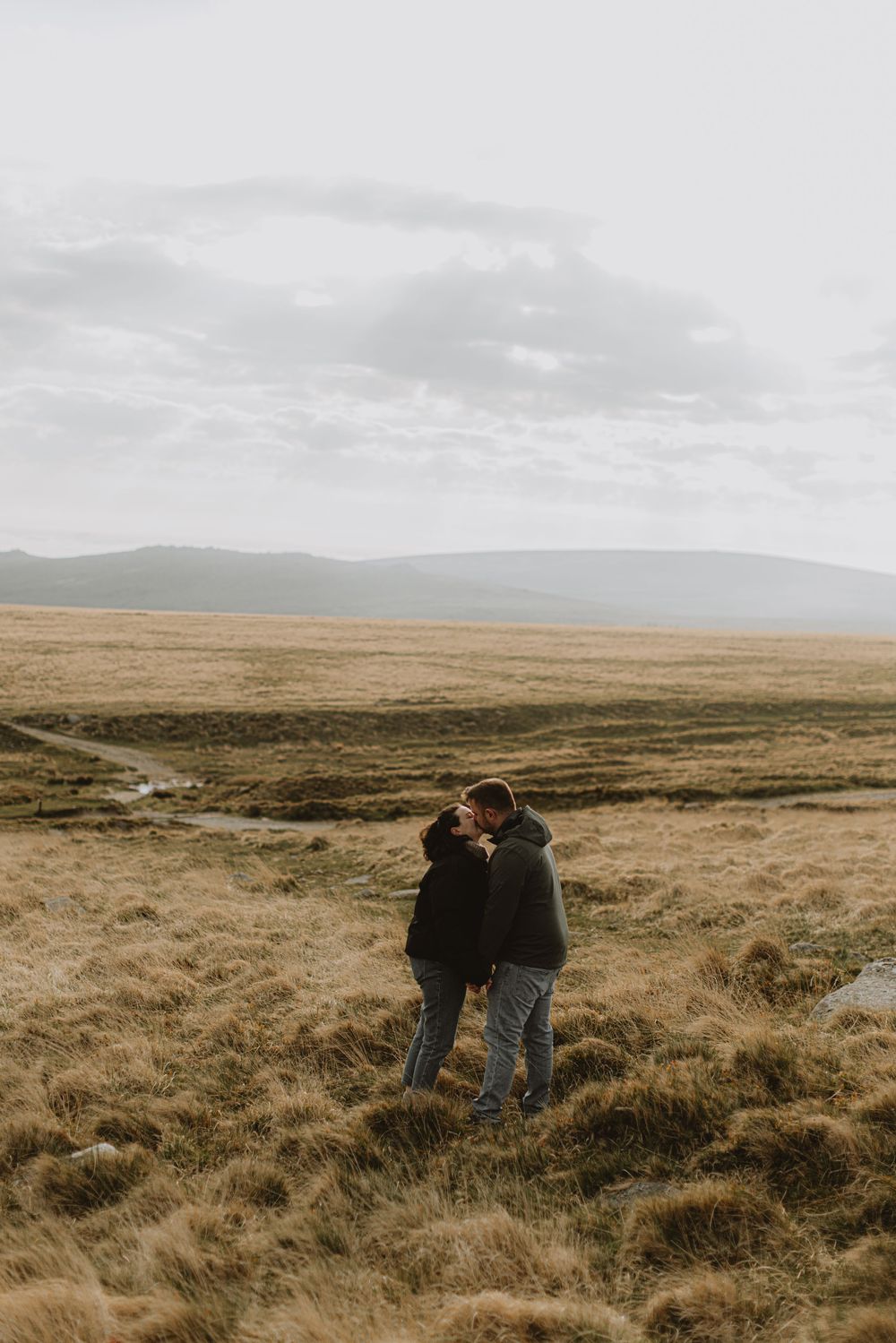 Couple overlooking vast moorland landscape under dramatic cloudy skies.