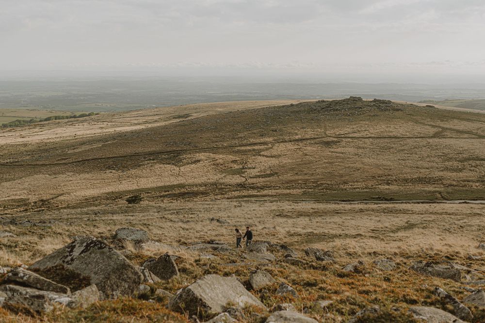 Two silhouettes walk along a rugged hilltop landscape under cloudy skies.