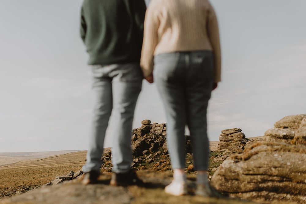 Two people stand at the edge of rocky terrain overlooking a vast landscape.
