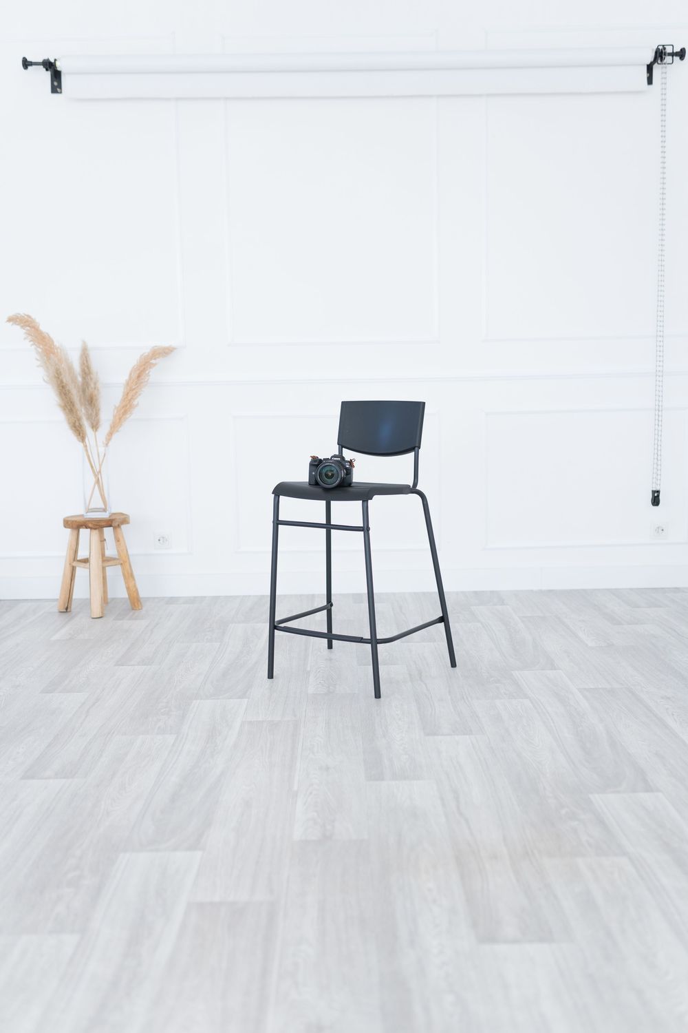 Minimalist black bar stool against white wall with pampas grass home decor accent on wooden side table.