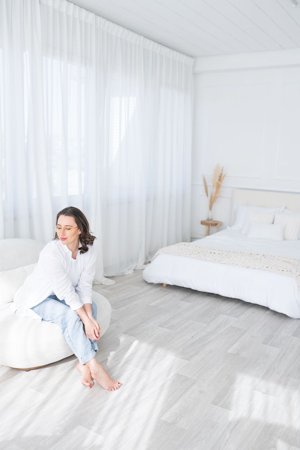 Bright white minimalist bedroom with flowing curtains and gray wood floors.