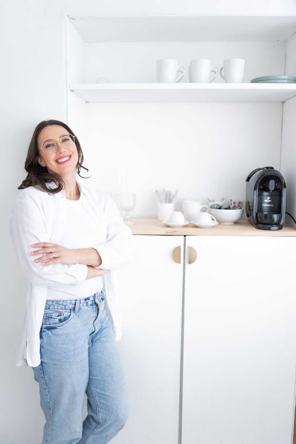 Casual professional relaxing in bright modern kitchen with coffee maker and shelving.