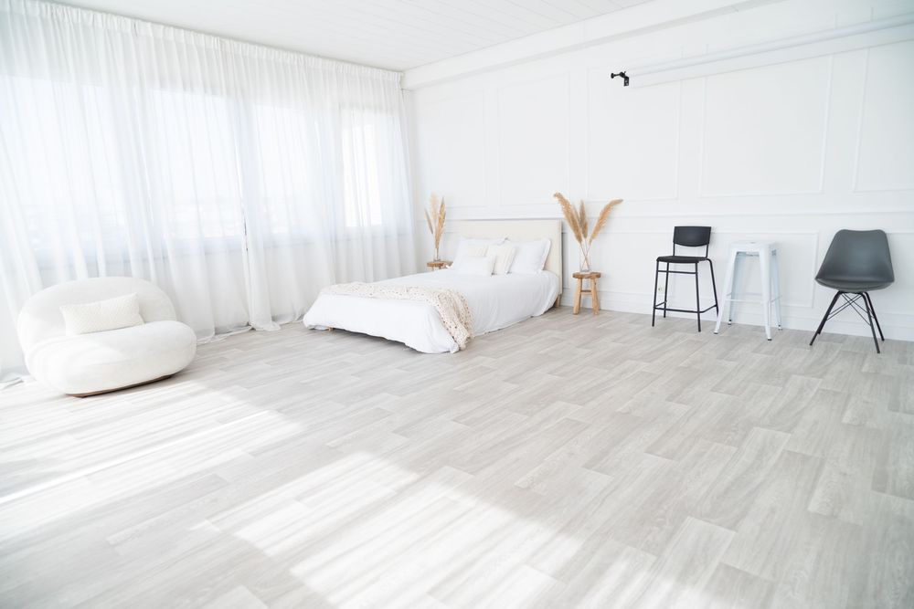 Minimal white photography studio with natural light, grey flooring, and scattered chairs and decorative elements.