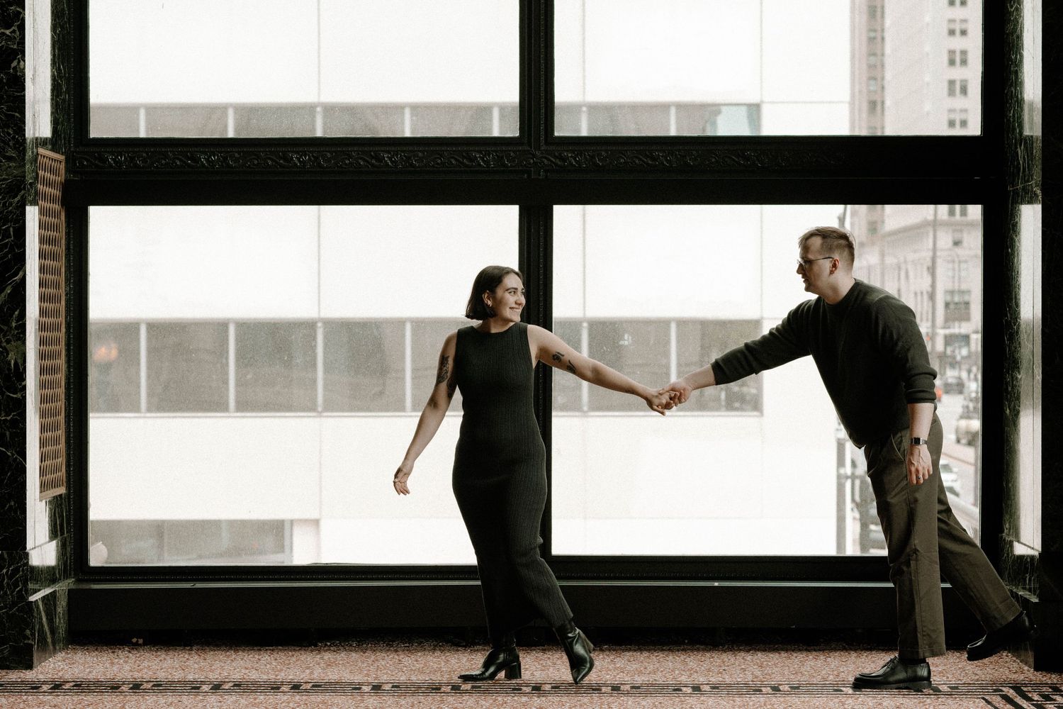 Two figures silhouetted in an elegant dance pose against bright window lighting in an indoor studio setting.