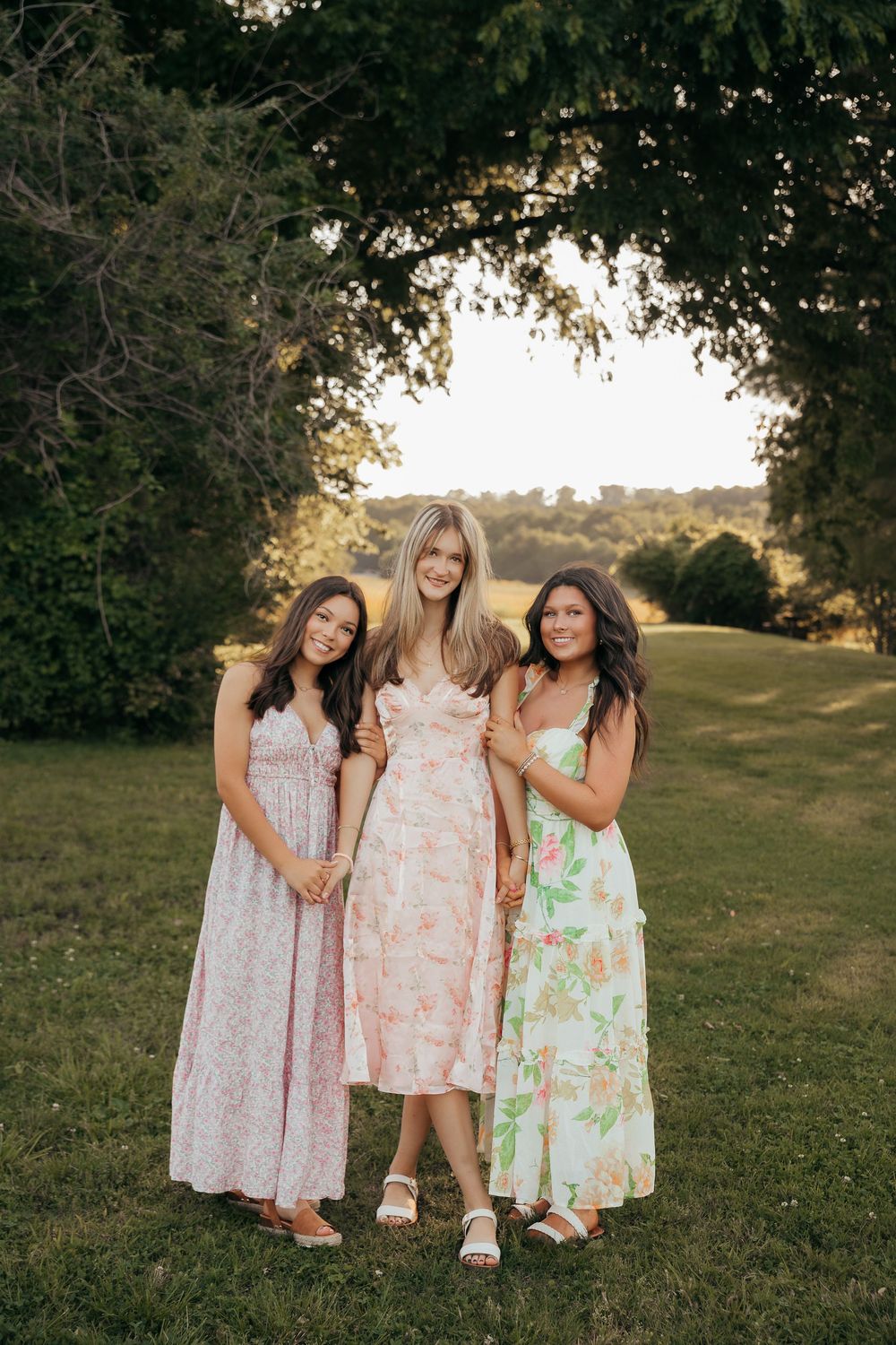 Group wearing floral summer dresses posing together in outdoor garden setting.