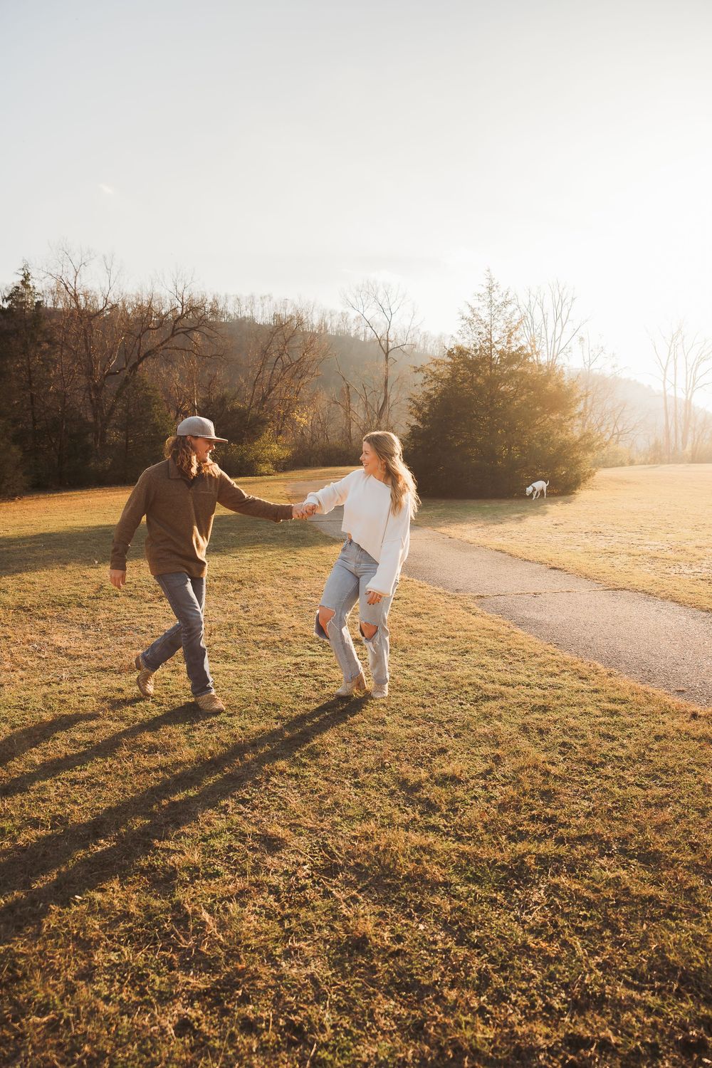 Couple running and holding hands in a sunlit field during golden hour.