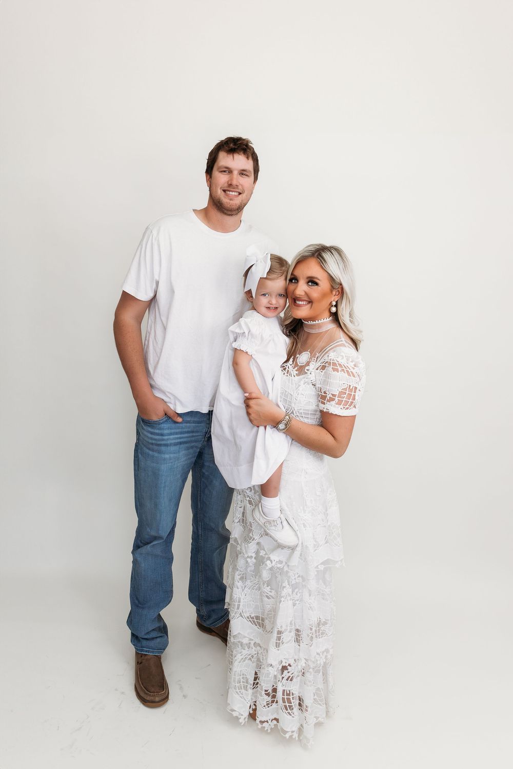 Family portrait session in all white outfits against neutral background.