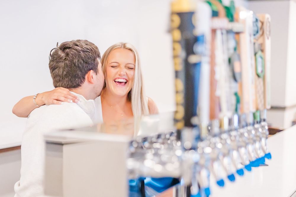 A couple shares a joyful moment together at a bar with beer taps in the background.