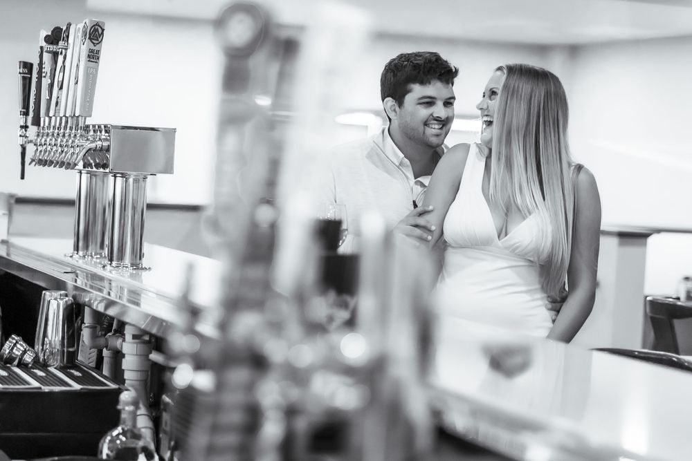 Black and white photo of a couple sharing an intimate moment at a bar near beer taps.