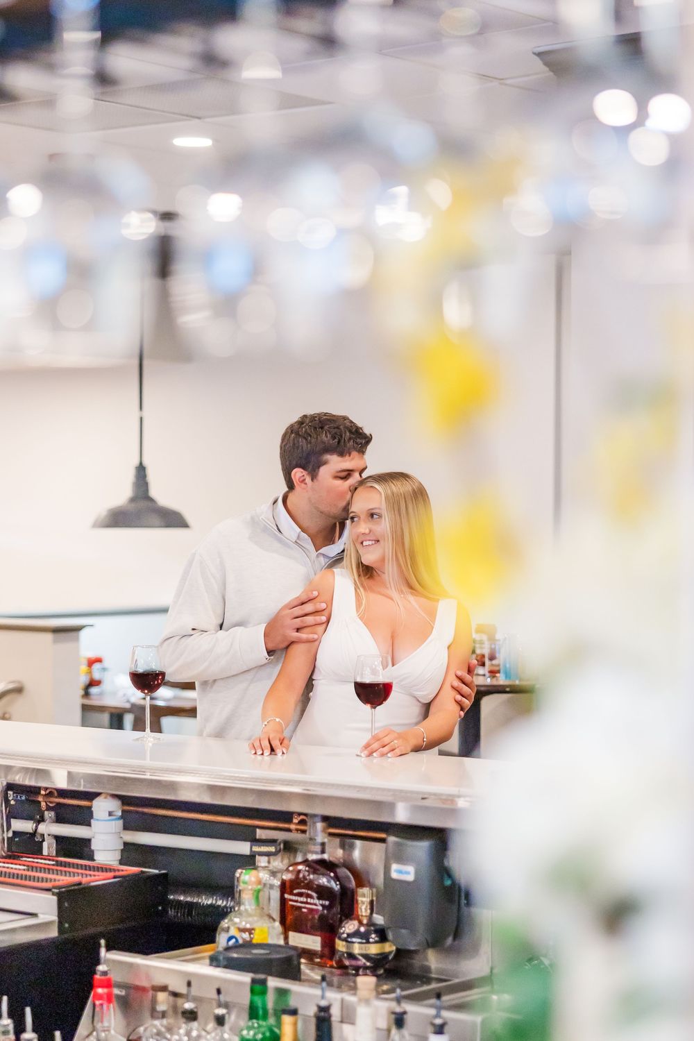 A couple enjoying wine and conversation at a bar with bokeh lights overhead.