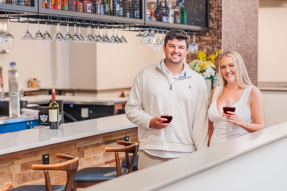 A couple holding wine glasses while standing together at a rustic bar counter.