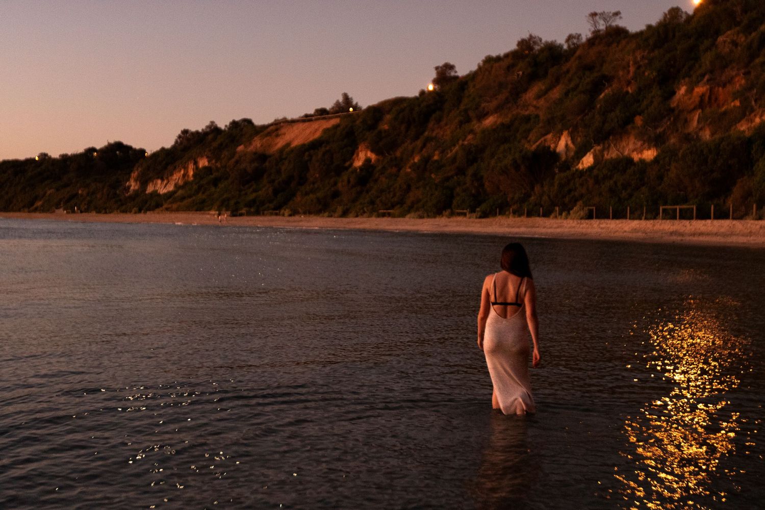 Silhouette of person in dress standing in calm ocean waters at sunset.