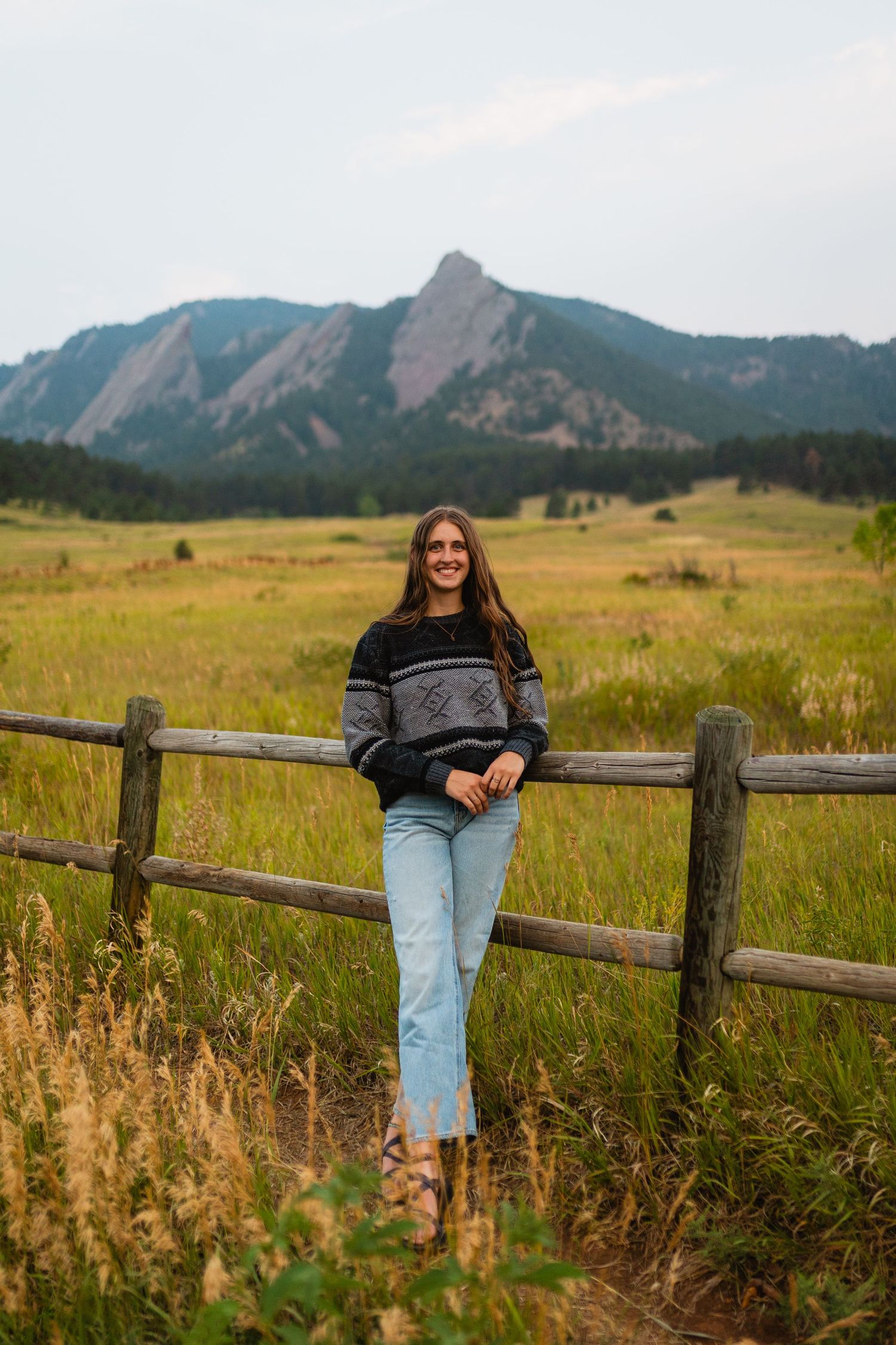 Scenic mountain landscape in Boulder, Colorado with person sitting on wooden fence surrounded by golden prairie grass.