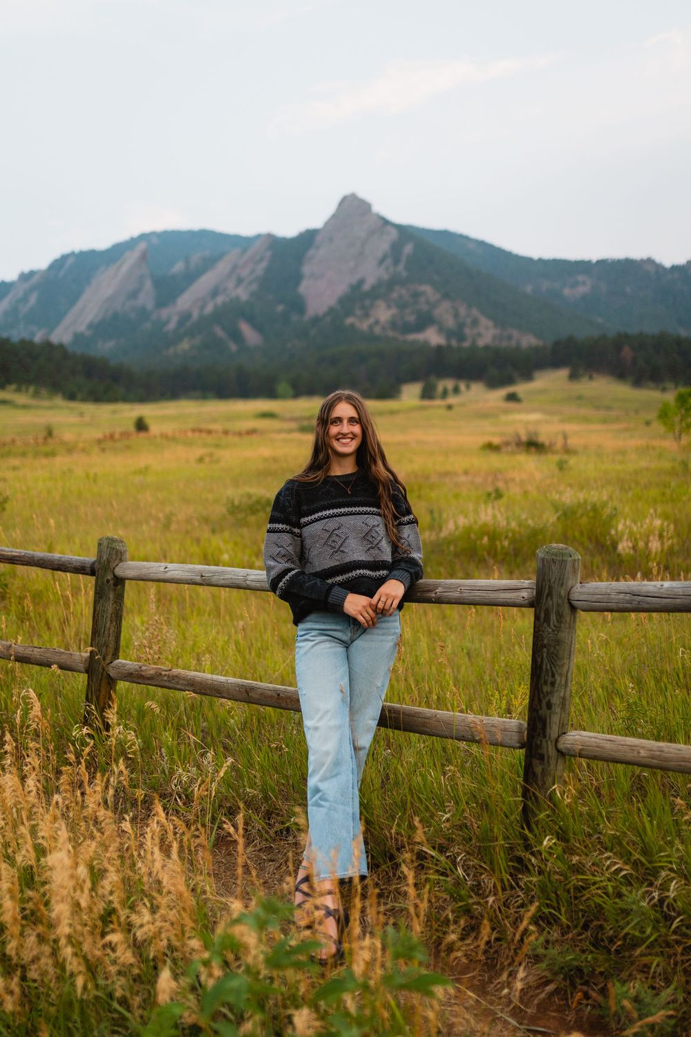 Scenic mountain landscape in Boulder, Colorado with person sitting on wooden fence surrounded by golden prairie grass.