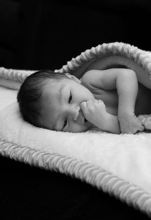 Newborn baby lying on a soft white blanket with fist near mouth in a peaceful black and white portrait.