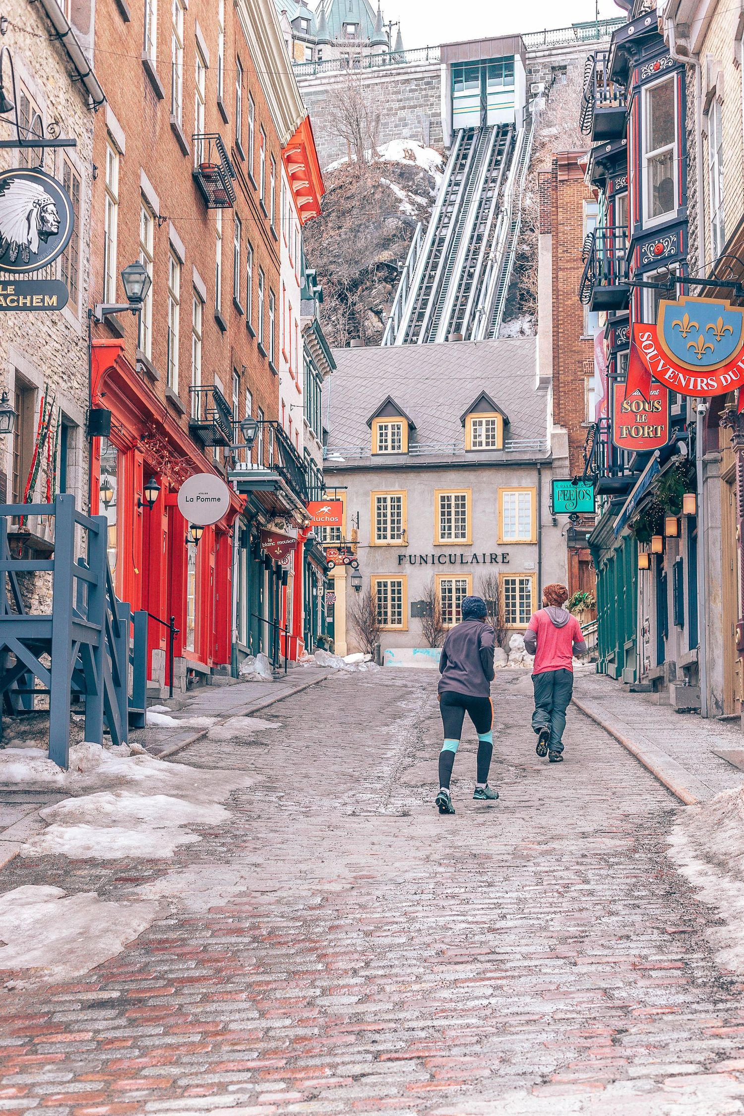 Steep cobblestone street in Quebec City with funicular railway visible in the background.