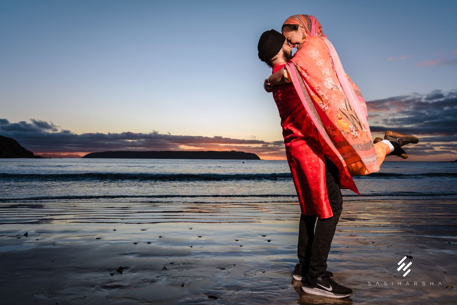 Figures in bright clothing pose dramatically on beach at sunset.