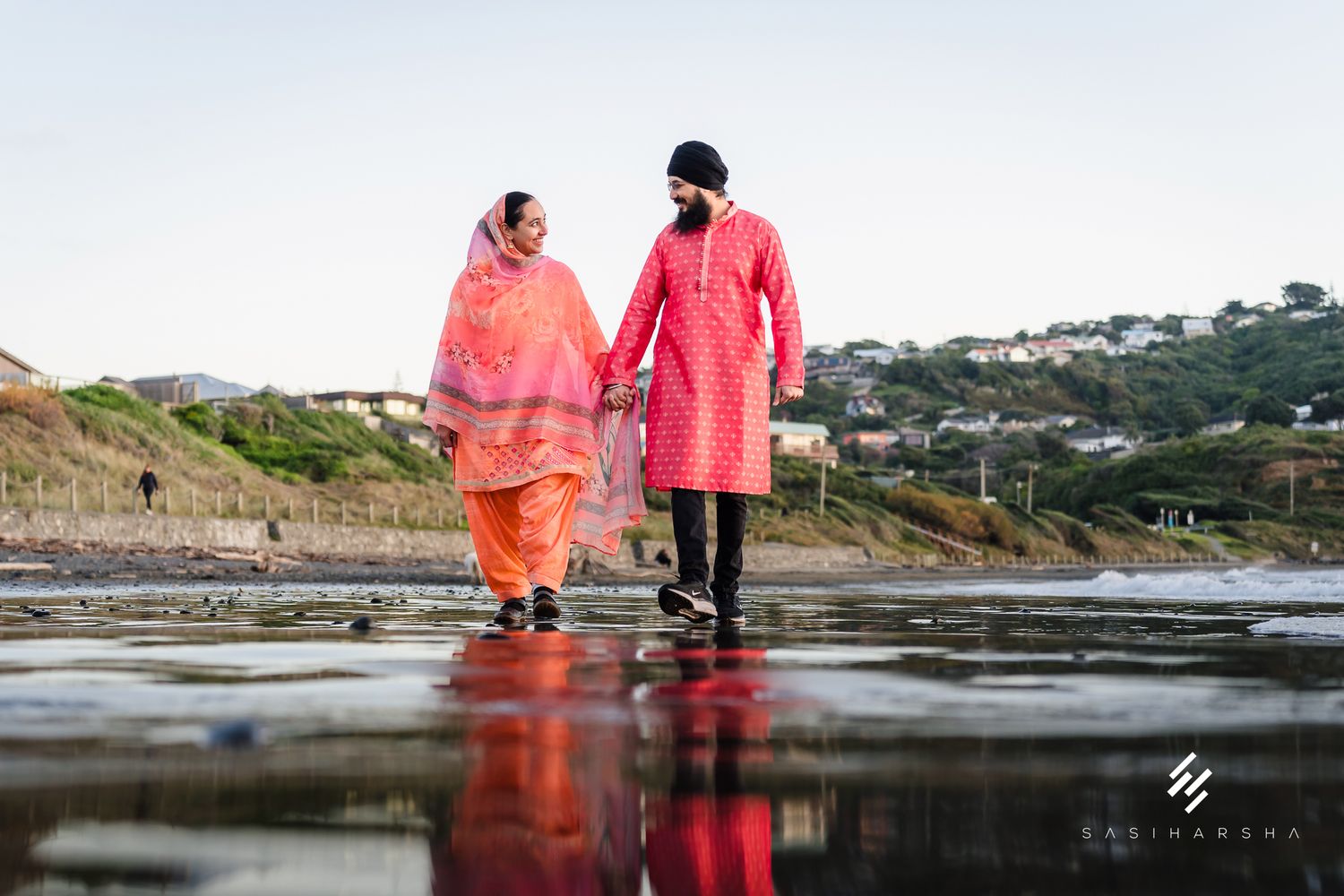 Two figures stand reflected in tidal pools along a rocky beach.