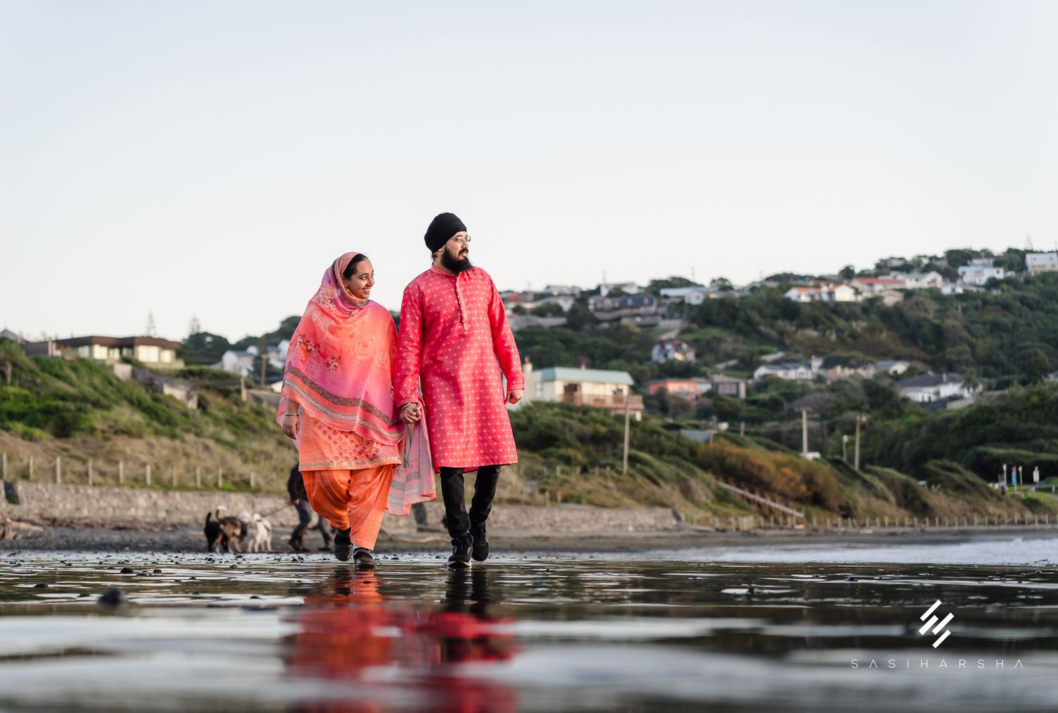 Couple walks along rocky shoreline with colorful fabric flowing in the wind.