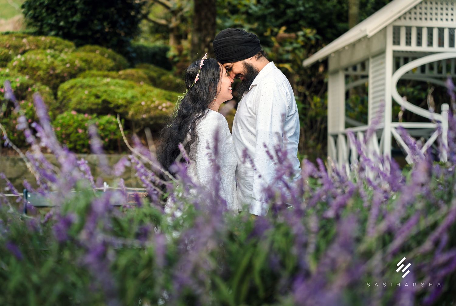A romantic moment captured among blooming purple flowers with a white gazebo in the background.