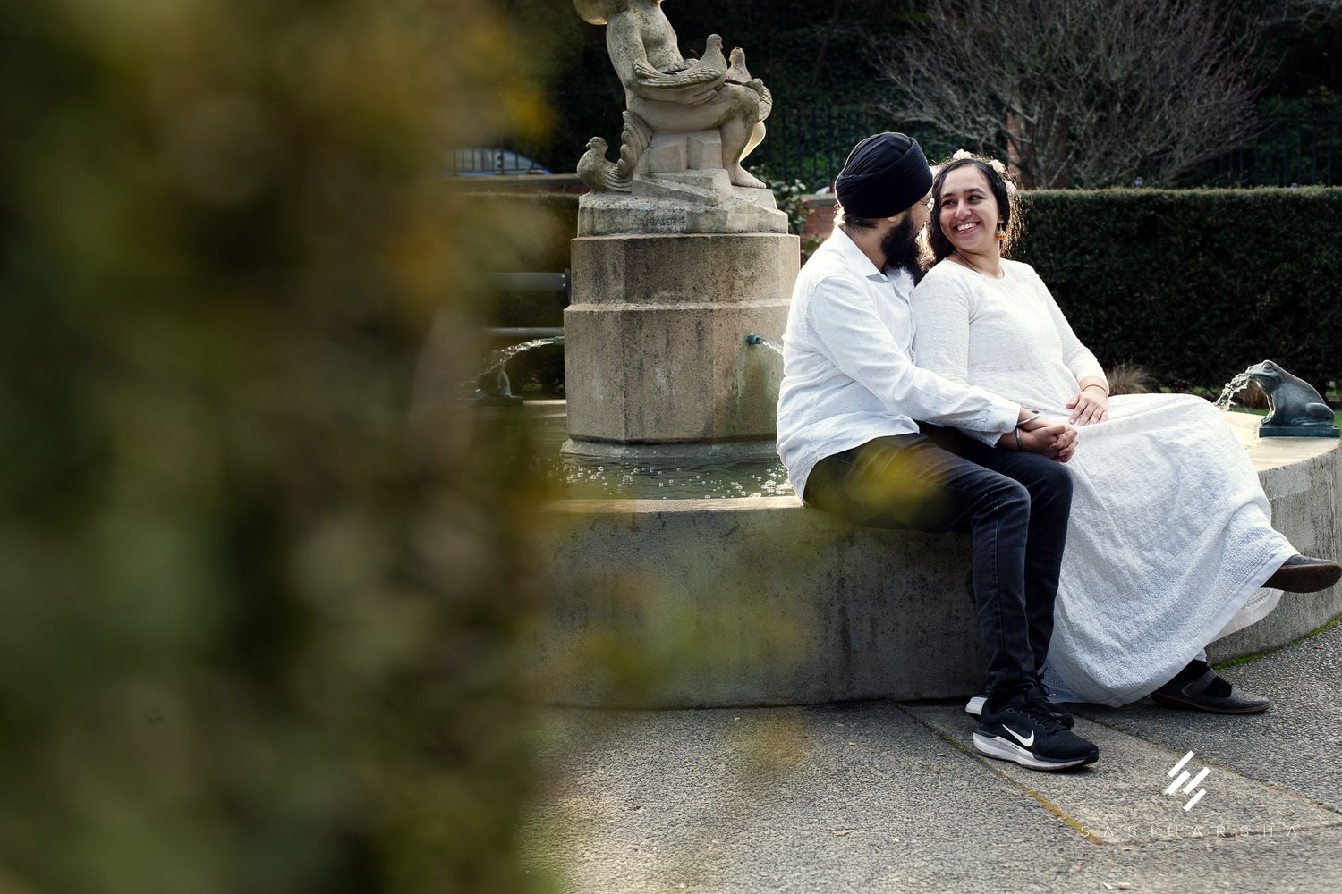 A couple sits together on stone steps near a decorative garden statue.