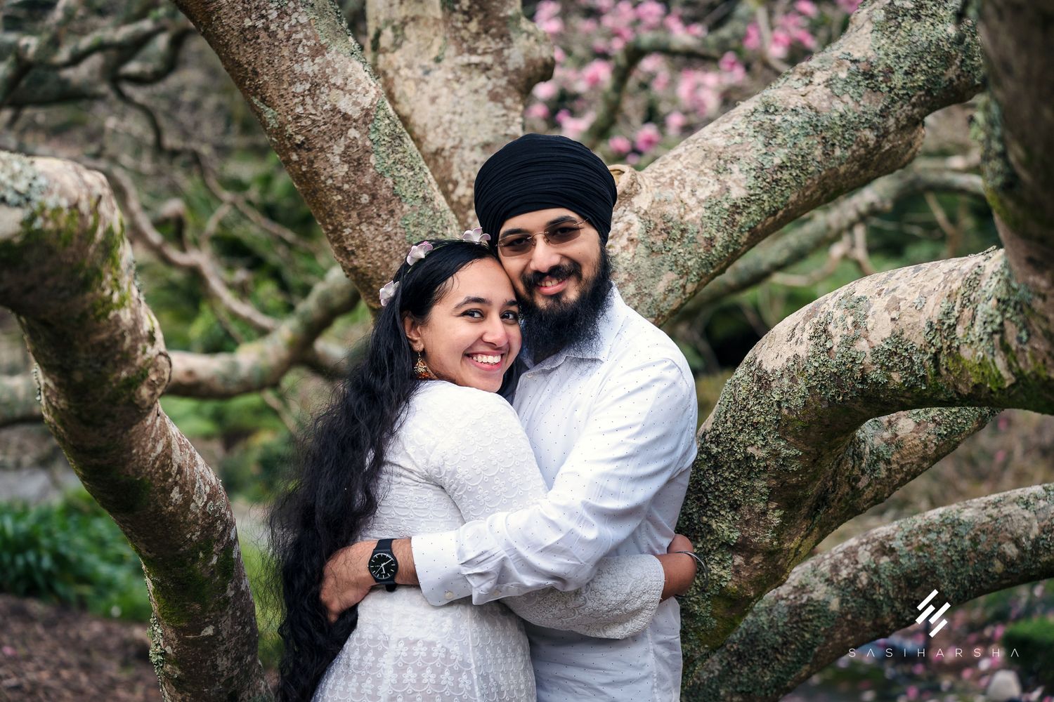 A couple shares an intimate moment while standing beneath a flowering magnolia tree.